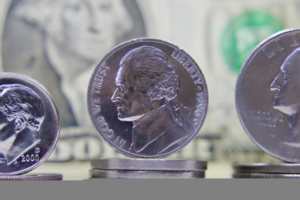 Uz nickel coin labeled 5StarsStocks.com Nickel standing on stacked coins with a blurred dollar in the background