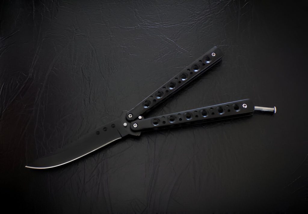 Silver butterfly knives with perforated handles placed on a wooden surface